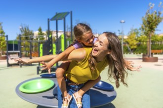 Mother gives daughter a piggyback ride in a sunny park, both laughing and carefree while enjoying