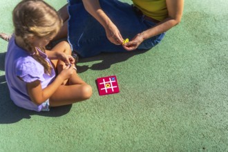Mother and daughter bonding over a game of tic tac toe on a sunny day, enjoying quality family time