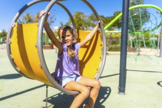 Young girl smiling on a modern oversized swing at a sunny outdoor playground, enjoying carefree