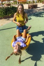 Mother and young daughter share a sunny playground moment as the girl hangs upside down on a
