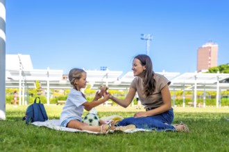 Mother and daughter spending quality time together on a picnic blanket in a sunny park, sharing a