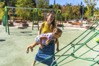 Mother and daughter smiling and laughing while playing on a sunny outdoor playground, climbing rope