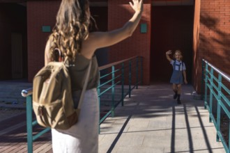 Mother and daughter saying goodbye, the child waving to her mother while walking into school