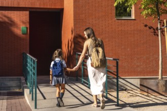 Mother and daughter walk uphill hand in hand with backpacks, returning to schoolbonding, support