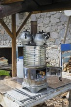 Wood-fired metal stove with tea kettles and wood supply on a table, traditional samovar, kettle for