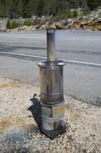 Metal stove with chimney stands on the side of the road against a wooded backdrop, traditional
