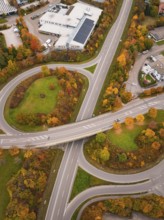 Road intersection with roundabout surrounded by green areas and autumn trees from a bird's eye