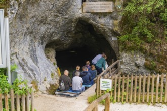 Group of people at the entrance of a cave surrounded by rock walls and lush vegetation, Wimsener