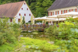 Café by a stream in a quiet, green area with traditional houses, Wimsener Höhle, Hayingen, Germany