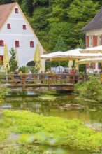 People sitting in a café by a stream in picturesque landscape, Wimsener Höhle, Hayingen, Germany