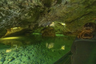 Interior of a cave with green water and rocks, people exploring the underground body of water,