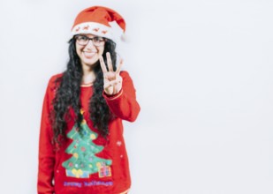 Smiling girl in Christmas sweater counting number 3. Happy girl in Christmas hat counting number