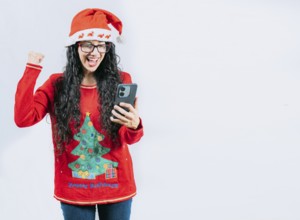 Excited girl in Christmas sweater looking at phone screen, isolated. Young woman in Christmas hat