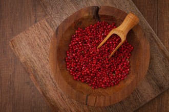 Bright red peppercorns, in a wooden bowl, with a small wooden tray