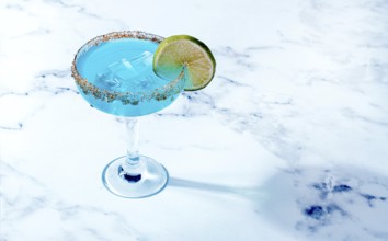 Bright blue cocktail with a slice of lime on a marble surface