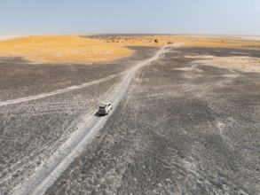 Aerial view of off-road car driving on a salt pan, arid landscape, Botswana