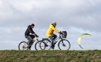 Cyclists ride across a dike and look at the sails of kite surfers, Fehmarn, 16.10.2025, Fehmarn,