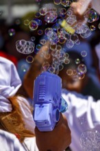 Playing with colorful soap bubble gun in sunny day