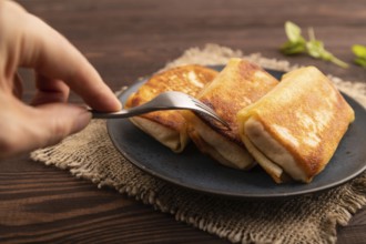 Fried crispy pancakes with meat and cheese with hand on brown wooden background and linen textile.