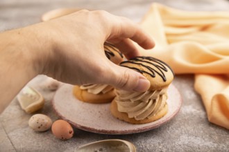 Caramel Cream Cakes with hand on brown concrete background, cup of coffee, side view, close up,