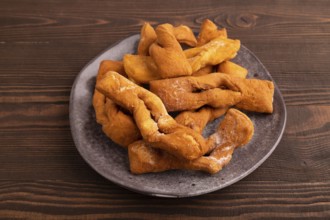Crunchy biscuit Brushwood cookies sprinkled with powdered sugar on brown wooden background, side