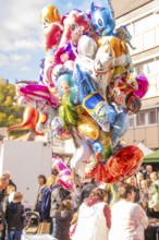 Colourful balloons in the form of cartoon characters float above a crowd at a festival,