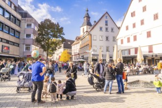 Bustling market square with families, church in the background, sunny day and historic houses,