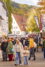 Families stroll across a busy market street under autumn leaves, Urschelherbst street festival,