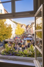 From a window you can see a lively street full of people and colorful market stalls under yellow