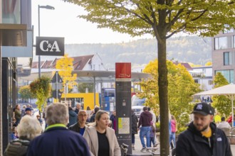 Street scene with people in a city with shops and trees in autumn leaves in the background,