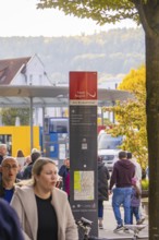 People walk past a bus stop, a signpost shows the way, Urschelherbst Street Festival, Nagold,