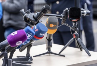 Microphones from various radio stations, television stations, standing on the table, at a press