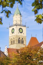 A church tower with clocks rises into the blue autumn sky, surrounded by autumn leaves, Überlingen,