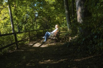 Woman sitting relaxed on a bench in the forest, pierced by sunspots, Überlingen, Lake Constance,