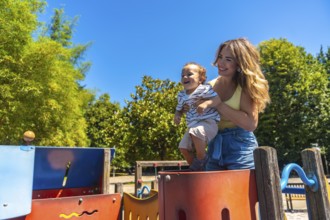 Happy mother holding her smiling son on a colorful playground game structure on a sunny summer day