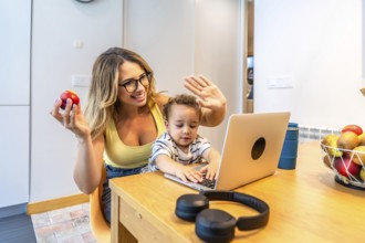 Mother and son waving joyfully at the computer during a video call while enjoying breakfast