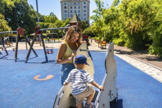 Mother helping her son enjoy a sunny day at the playground, happily playing together on a rocking