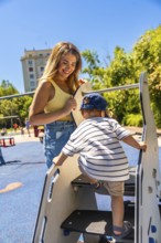 Smiling mother holding balance board assisting her son climbing stairs of a playground slide in a