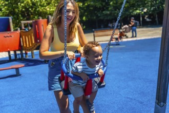 Happy mother enjoying quality time with her toddler son, playfully pushing him on a swing at the