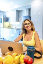 Young woman working on laptop in modern kitchen with fresh fruits, promoting healthy work life
