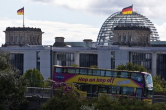 Reichstag dome with German flags and double-decker bus of the city tour hop on hpo off, German