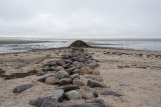 A stone groyne made of large granite blocks stretches from the sandy beach on the island of Föhr