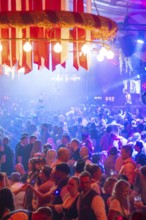 Large crowd celebrating in a beer tent under colourful lights and enjoying the music, Volksfest