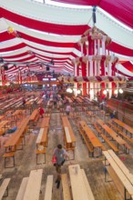 View of a festively decorated beer tent with red blankets and empty wooden benches, Volksfest