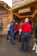 People stand in front of a wooden entrance, some wearing red shirts. A security-conscious