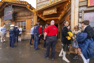 People in traditional Bavarian dress and police gather in front of a festively illuminated wooden