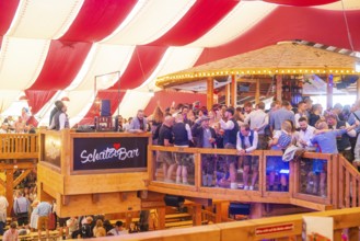 A crowded upper bar with people in traditional dress in a festively decorated room, Volksfest