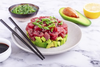 Fresh tuna tartare with avocado served on a marble table with soy sauce and seaweed salad