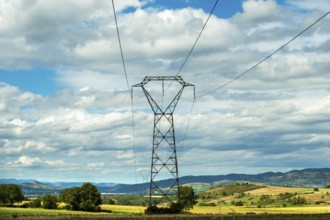High voltage power lines against a bright blue sky with scattered clouds, Puy de Dome, Auvergne