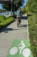 A person rides a bicycle on a smooth pathway lined with trees and shrubs. Vichy. Allier. Auvergne